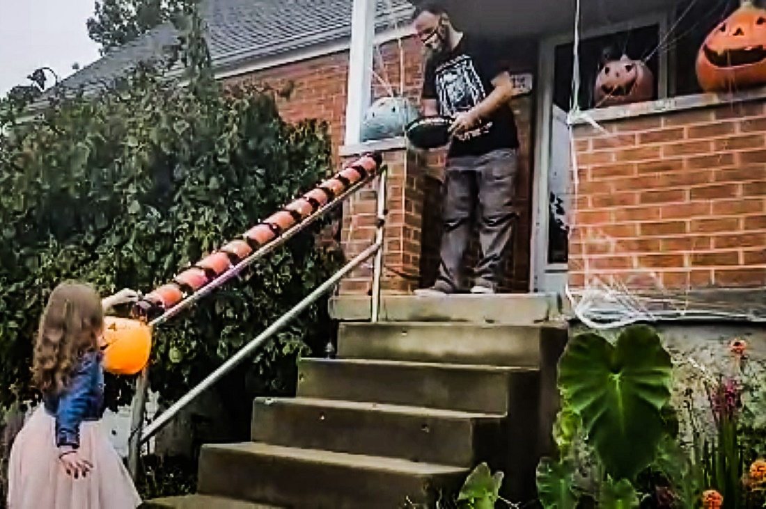 A homeowner gives Halloween candy at a safe distance to a trick-or-treater using a homemade &amp;quot;Halloween chute&amp;quot; attached to a hand rail next to front steps at a house.