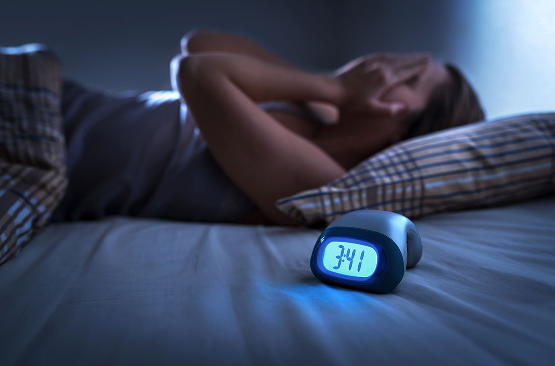 Woman holding her face in bed next to an alarm clock