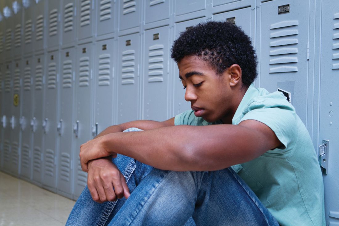 An African-American teenager sits in front of a row of lockers.