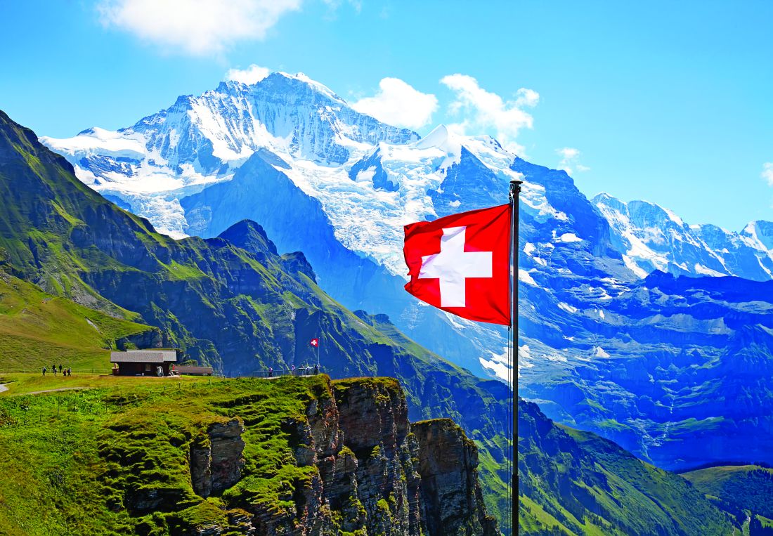 A picture of the Switzerland flag flying in the Swiss mountains.