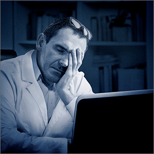 Man sitting at computer holding head in front of bookshelf