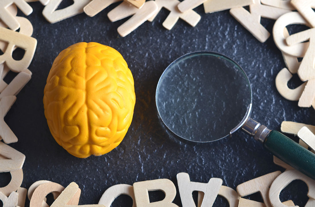 Brain next to magnifying glass with wooden letters surrounding