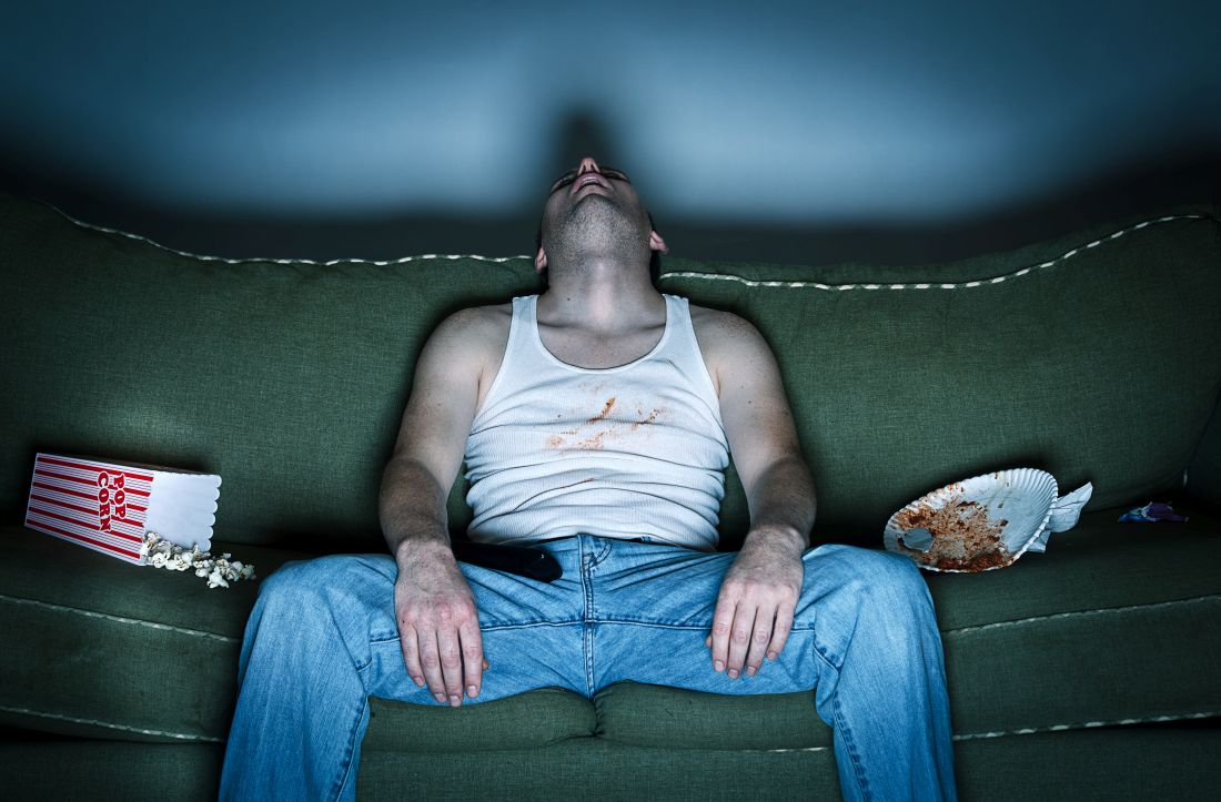 A man sleeps in upright position on his couch.