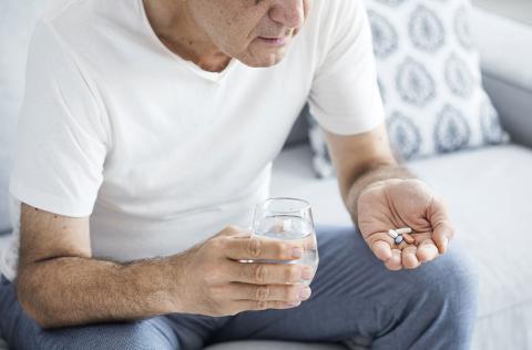 Man sitting on couch with pills and glass of water in hands