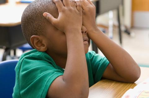 Child sitting at desk covering eyes with hands