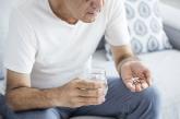 Man sitting on couch with pills and glass of water in hands