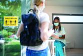 Female teen approaches a check in nurse. Covid safe distancing poster on window.