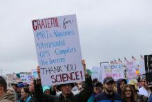 A man holds up a sign that outlines why he is grateful for science. He is surrounded by a crowd; many others have signs.