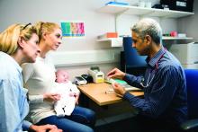 A woman holds her baby while accompanied by her mother, as a physican talks to them.