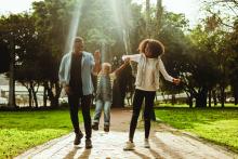 Happy beautiful family of three walking in park. Happy couple in playful mood outdoors enjoying with their child.