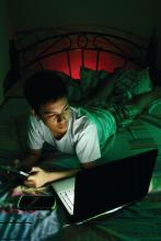 Teenager on his bed, looking at a laptop computer.