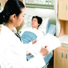 A doctor writing notes while a patient sleeps in a hospital bed