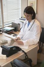 Photo of a female doctor sitting at her desk review information on a tablet.