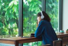 Woman listening to music with headphones near window at a restaurant.