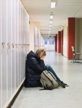 Teen sitting on floor in hallway at school