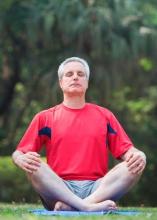 A man sits cross-legged in the grass, meditating.