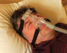 Sleep apnea sufferer being treated by CPAP via mask and air tube from machine.