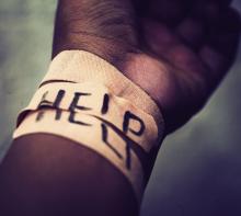 A wrist is shown wrapped in adhesive bandages with the word &quot;HELP&quot; spelled out across them.