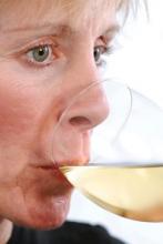 woman in her 40s drinking a glass of white wine.