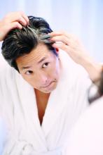 Asian man looking at his gray hair in mirror