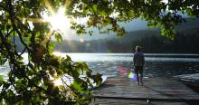 Man walks onto dock over lake and watches sunrise over mountains and forest