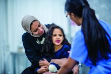 Mother and daughter are indoors in a hospital. The daughter is about to have a checkup. Her mother and doctor are trying to comfort her.