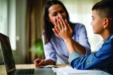 Mother giving high five to son at table with laptop and papers