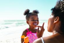 Black mother applying sunscreen on Black girl