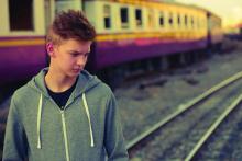 Teenager boy near train tracks looking moody.