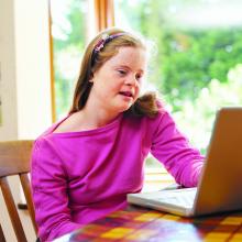 Teenage girl with Down syndrome working on a laptop computer.