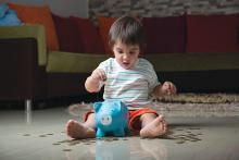 Young child sitting on the floor and putting a coin into a piggy bank.