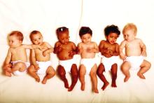 Different race babies laying in a line in diapers.