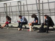 People sitting on a bench look at their smartphones.