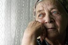 An elderly woman who is depressed looks out a window