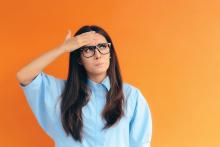 A woman with a quizzical look holds her hand to her forehead