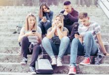 A teenager surrounded by her friends who are staring at their smartphones