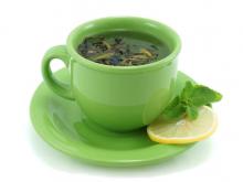 A cup of green tea with a lemon on the side