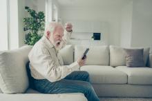 old man with a beard on a sofa, yelling at his cell phone