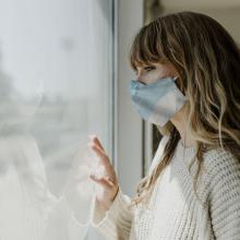 Woman wearing mask looks out through window