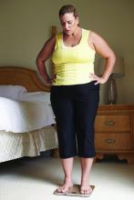 An obese woman weighs herself on a scale at home.