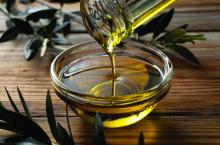 The moment olive oil is poured into a glass bowl set against a wooden background