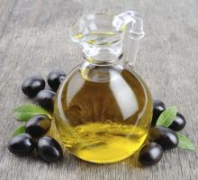A bottle of olive oil surrounded by black olives