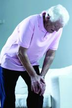 An older man bends over in pain with his hands on his left knee.