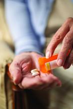 An older woman slides two pills from her prescription bottle onto her palm.