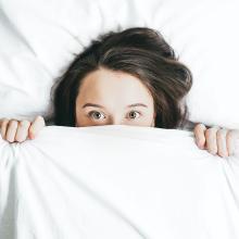 A woman peeks out from under a blanket