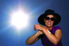A woman wearing a wide-brimmed hat applies sunscreen to her arm.
