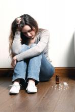 Depressed teen girl sitting on floor with pills